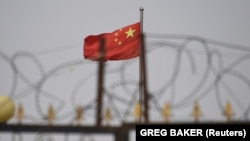Флаг Китая на фоне колючей проволоки в местности близ Кашгара, города в Синьцзяне.