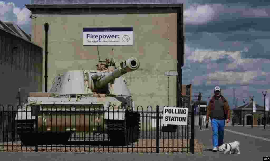 A man walks his dog past a tank with a Howitzer gun outside the Greenwich Heritage Centre, set up as a polling station for Britain&#39;s general election in London on May 7. (AFP/Daniel Sorabji)