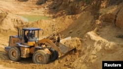 Hytaýdaky seýrek duş gelýän ýer metallary käninde işçi ýük göteriji bilen topragy süýşürýär.