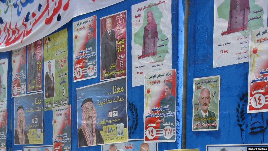 An Iraqi police officer in front of campaign posters on blast wall outside a Baq'ubah polling station