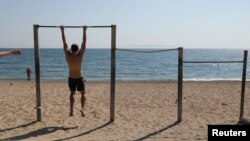 Мужчина делает упражнения на турнике на пустынном пляже в Афинах (Греция). 28 апреля 2020 года.