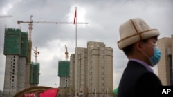 Мужчина в калпаке (кыргызском национальном головном уборе) в Урумчи на фоне строящихся зданий. Фото сделано во время организованного властями визита иностранных журналистов в Синьцзян. 22 апреля 2021 года
