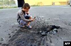 Un copil fotografiază impactul unei bombe în asfalt în Donețk.