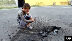 A young boy takes a picture of a crater left in the asphalt in the eastern city of Donetsk.