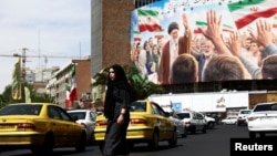 27-nji aprelde Tähranda bir aýal Eýranyň aýatdan öten ýokary ruhany lideri Aýatolla Ali Hameneýiniň suraty goýlan bilbordyň ýanyndan geçip barýar.