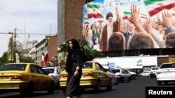 A woman walks past a billboard featuring an image of late Supreme Leader Ayatollah Ali Khamenei in Tehran on April 27.