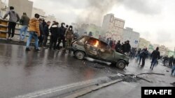 Iranian protesters stand around a vehicle set ablaze during clashes in Tehran on November 16, 2019.