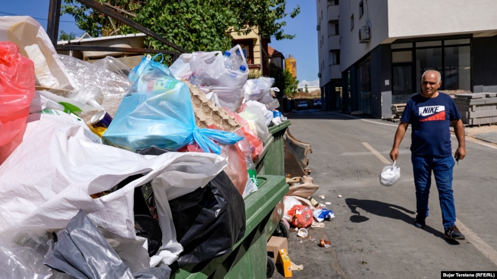 Rafet Berisha duke hedhur mbeturina në kontejnerët e stërmbushur në Fushë Kosovë. Ai i tha Radios Evropa e Lirë në shtator se trotuaret janë të bllokuara nga makinat, ndërsa grumbuj mbeturinash shihen pothuajse në çdo lagje.Menaxhimi i keq i mbeturinave është ndër telashet e përditshme që përballen banorët e kësaj komune pranë kryeqytetit.