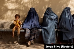 A girl sits with women wearing burqas outside a hospital in Kabul on October 5.