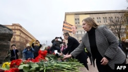 Foreign diplomats, including the U.S. Ambassador to Russia Lynne Tracy (right foreground), lay flowers at a monument to victims of political repressions in front of the former KGB headquarters in Moscow on October 30. A pro-Kremlin activist holding a flag with a portrait of Russian President Vladimir Putin stages a picket nearby. 