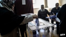 A woman casts her ballot in Istanbul as electoral workers look on in Turkish local elections on March 30.