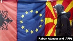 A man walks by Albanian EU, and Macedonian flags displayed in a bazaar in Skopje.