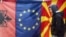 A man walks by Albanian EU, and Macedonian flags displayed in a bazaar in Skopje.