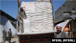 یک کارگر در حال پائین کردن بوری های آرد از یک موترباربری در شهر میمنه مرکز ولایت فاریاب