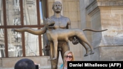 People take photos next to the much-mocked statue in Bucharest.