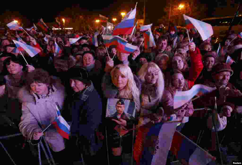 A woman holds a portrait of Russia's President Vladimir Putin as others wave Russian flags as the preliminary results of referendum on Crimea joining Russia are announced on March 16. (Reuters/Baz Ratner)