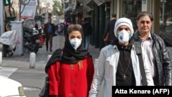 People wearing protective masks walk along a street in the Iranian capital, Tehran, on February 24.