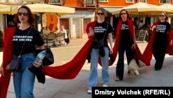Участники акции протеста против участия РФ в биеннале несут ткань кровавого цвета