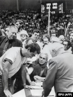 Henry Iba (left), the coach of the U.S. team, looks over the shoulder of a referee as he explains to officials the circumstances that put an extra three seconds back on the clock.