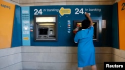 Уборщица стирает пыль с банкомата перед входом в отделение Bank of Cyprus в Никосии, 28 марта 2013