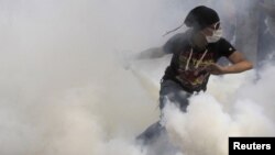 An antigovernment protester runs to throw a tear-gas canister back during clashes with Egyptian riot police on Tahrir Square in Cairo on November 27.