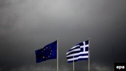 Greece -- EU and Greek flags fly in front of dark rain and thunderstorm clouds in Athens, 10Oct2011