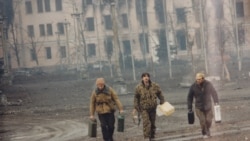 Chechen rebels walk with canisters near the presidential palace.