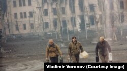Chechen rebels walk with canisters near the presidential palace.