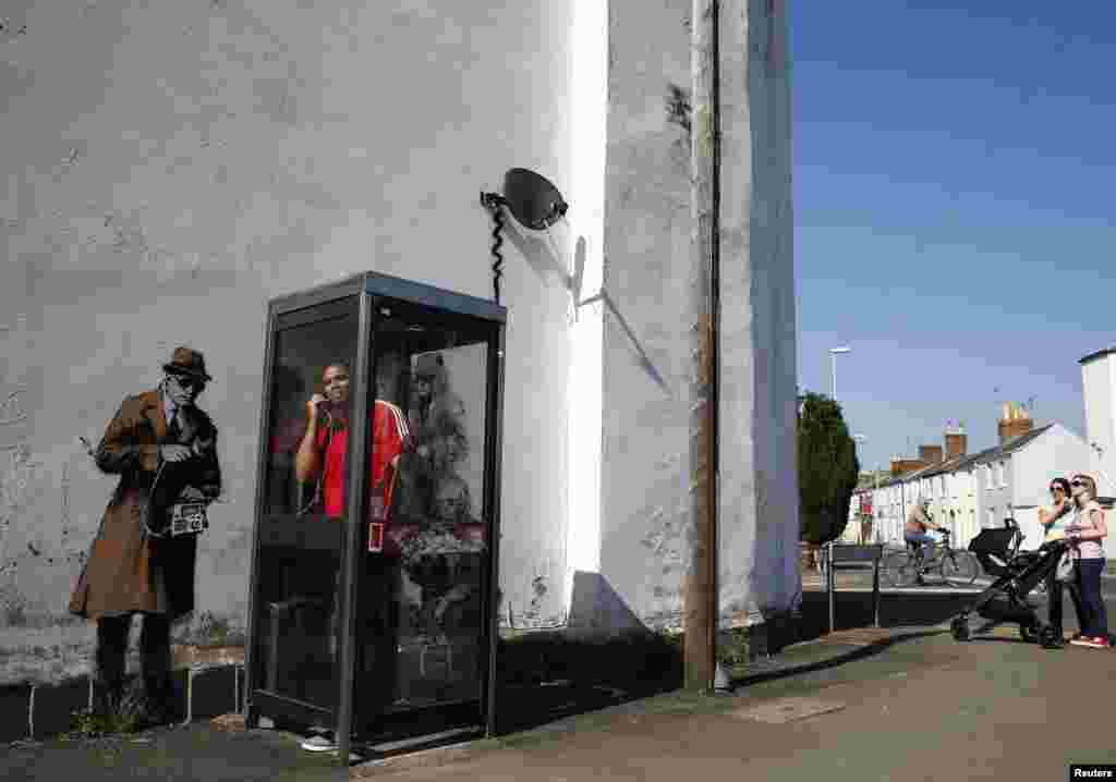 A man stands in a phone box in front of graffiti art on a wall near the headquarters of Britain's eavesdropping agency, the Government Communications Headquarters (GCHQ), in Cheltenham. (Reuters/Eddie Keogh)