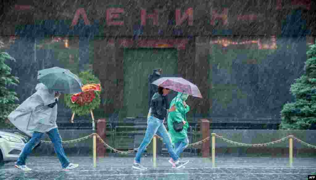 Pedestrians protect themselves from the rain as they walk past Lenin&#39;s tomb in Red Square in Moscow. (AFP/Dmitry Serebryakov)