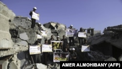 Syrian Civil Defense members, also known as the White Helmets, stand in protest on August 22, 2017 on the rubble of buildings in Zamalka, near Syria's capital Damascus