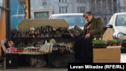 Təklifin sığortalanması: Tbilisidə küçə satıcısı yaz gülləri ilə yanaşı, qış geyimləri təklif edir. Levan Mikadze-nin fotosu
