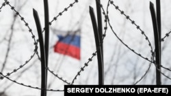 Российский флаг виден за колючей проволокой на заборе посольства России в Киеве