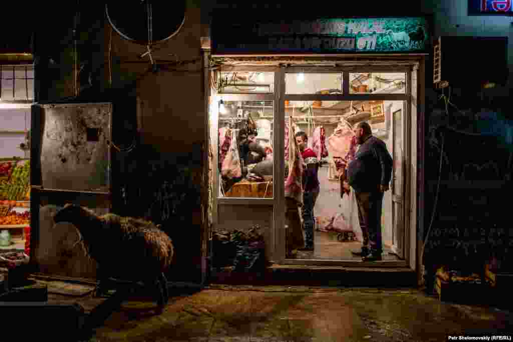 A sheep stands outside a butcher shop