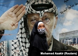 یک زن فلسطینی در حال عبور از دیوارنگاره‌ای با تصویری عرفات در حاشیه بیروت