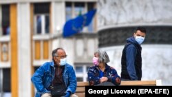 Një çift, që barti maska për t'u mbrojtur nga koronavirusi, qëndrojnë të ulur në një stol në qendër të Shkupit. Maj, 2020.
