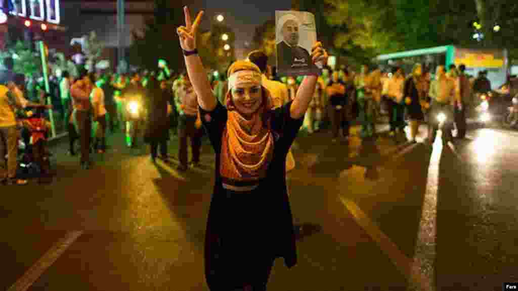 A woman flashes a victory sign alongside a photo of Rohani, a former military commander and lawmaker.