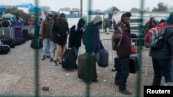 Migrants with their belongings queue at the start of their evacuation and transfer to reception centers in France, and the dismantlement of the camp called the "Jungle" in Calais on October 24.