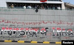 Protesters stand on top of a wall in Baghdad painted in slogans. November 1, 2019