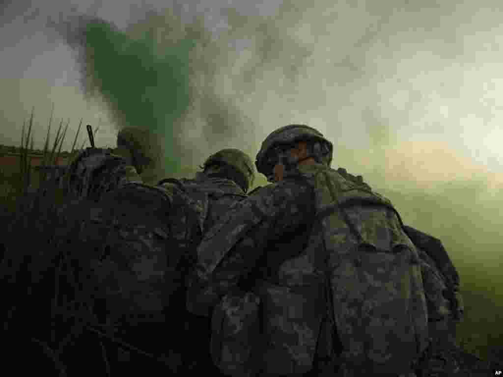 U.S. Army soldiers shield themselves from rotor wash as they use green smoke to mark a landing zone for a Black Hawk helicopter after an operation to disrupt weapons smuggling in Istaqlal, north of Baghdad, Iraq, on August 8. Photo by Maya Alleruzzo for AP