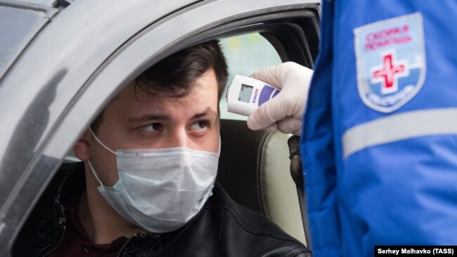 Сотрудник «скорой помощи» измеряет температуру водителю на блокпосту при въезде в Севастополь, апрель 2020 года