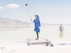 A photo from Maximilian Mann’s Finding Flamingoes series shows a woman shooting a selfie on the shore of Lake Urmia. Flamingoes that once populated the shallows of the lake have largely disappeared.