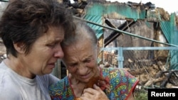 Women react while standing in front of the ruins of a burned house on the outskirts of the city of Voronezh.