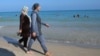 Women walk on a beach wearing burkinis.