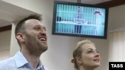 Russian opposition leader Aleksei Navalny and his wife, Yulia, laugh during a video-link with his brother Oleg, shown on a screen, in a court in Moscow on February 17.