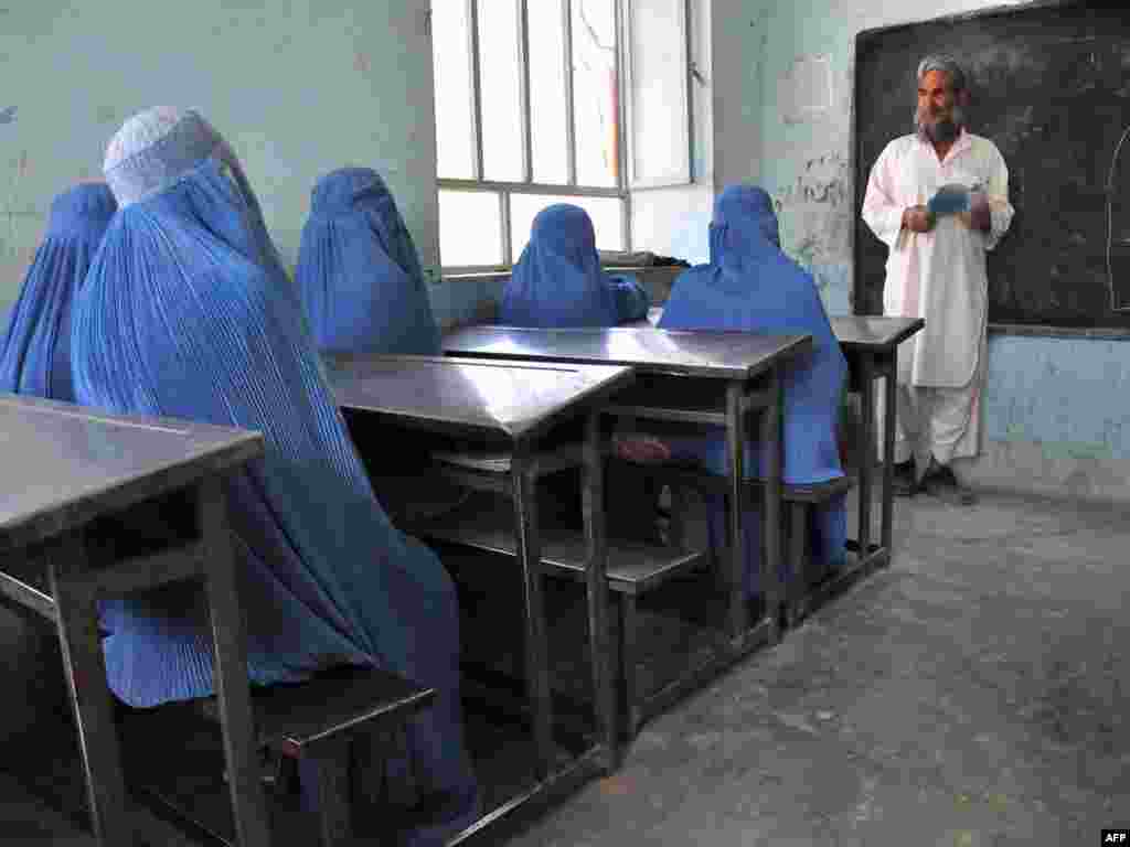 Schoolgirls in burqas listen to their male teacher in the outskirts of Afghanistan's Herat Province.