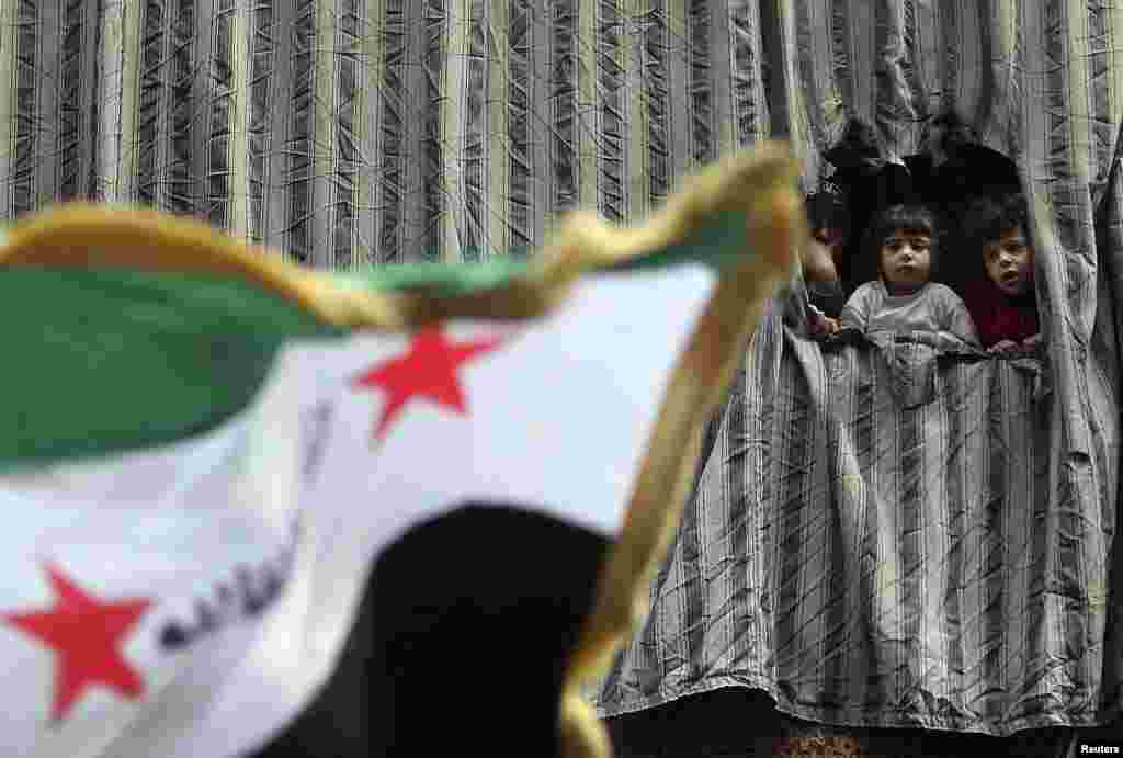 A woman and children stand on a balcony as they watch people protesting against Syria's President Bashar al-Assad in Aleppo. (Reuters/Muzaffar Salman)
