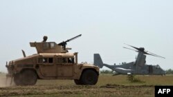 Un vehicul Humvee al armatei americane stă lângă o aeronavă MV-22B Osprey în timpul exercițiului militar „Platinum Eagle 15” la unitățile de antrenament din Babadag, 26 mai 2015.