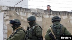 A Ukrainian serviceman peers over a wall at uniformed men, believed to be Russian servicemen, standing guard at a Ukrainian military base in the village of Perevalnoye, outside the Crimean capital, Simferopol, on March 6.