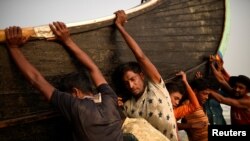 FILE: Rohingya refugees push a fishing boat from the sea at Shamlapur beach in Cox's Bazar, Bangladesh in March.
